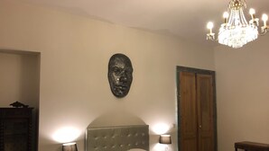 Une chambre à coucher avec une tête de lit capitonnée, deux lampes de chevet, un lustre, une armoire en bois et un élément décoratif en pierre sur le mur.
