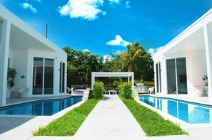 Une maison moderne dotée d’une piscine, de deux espaces de vie distincts et d’un patio couvert.