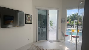 Una sala de estar moderna con un televisor de pantalla plana grande, un tapete con estampado de cebra y una puerta de cristal que da a una zona de piscina exterior con sillones de descanso.
