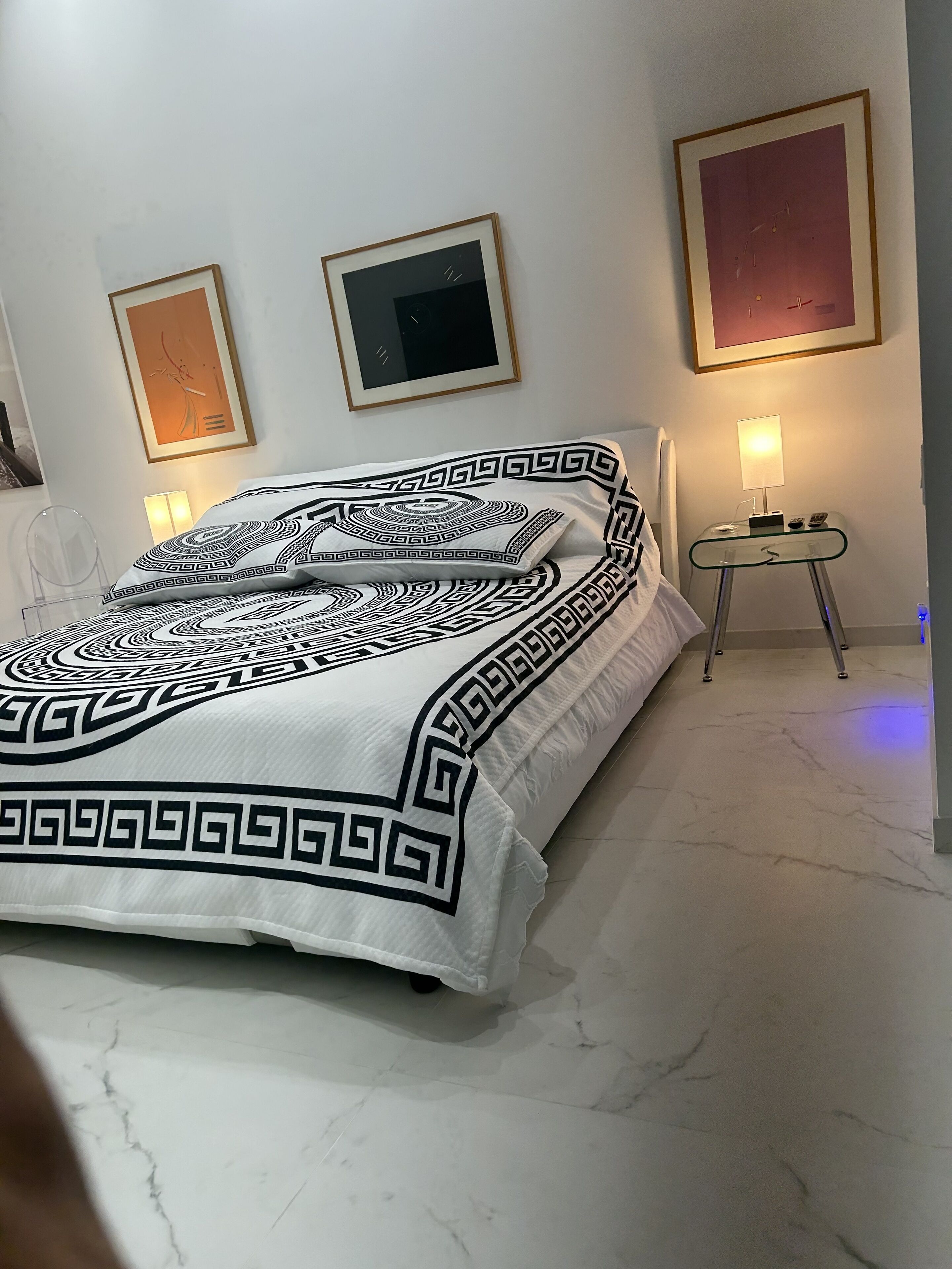A neatly made bed with a patterned bedspread, a bedside table with a lamp, and two framed artworks on the wall.