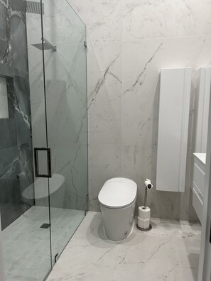 Une salle de bain moderne dotée d’une douche à parois de verre, de toilettes et d’un bidet.
