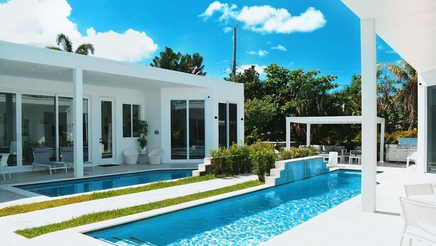 Una casa moderna con piscina, mobiliario exterior y abundante vegetación.