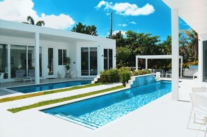 A modern house with a swimming pool, outdoor seating, and lush greenery.