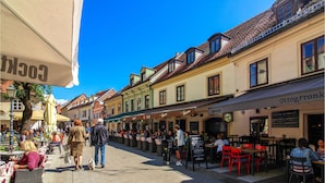 Une rue animée, bordée de cafés et de restaurants avec des terrasses, un ciel d’un bleu éclatant et une architecture européenne traditionnelle.