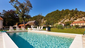 Une piscine rectangulaire à l’eau d’un bleu limpide, entourée de chaises longues blanches et d’une pelouse.