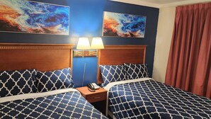 Habitación de hotel con dos camas, una mesita de noche con lámpara y dos cuadros abstractos en la pared.