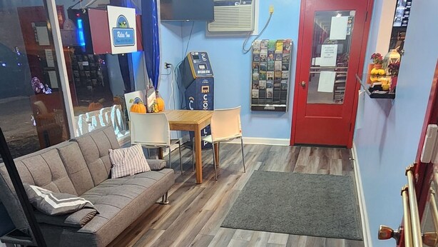Una habitación con suelo de madera, un sofá, una mesita, una puerta roja y una ventana con cortinas.