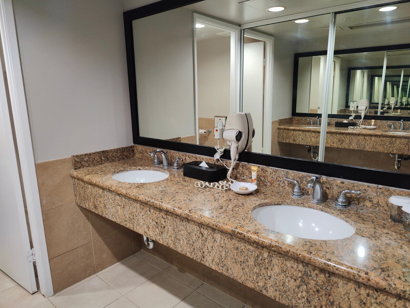 Un baño de hotel con dos lavamanos, un secador de pelo y un espejo grande.