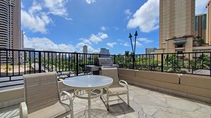 A balcony with a round table and chairs, a grill, and a view of the cityscape. - Large Studio w/ Pool sleeps six in comfort PLUS FREE PARKING INCLUDED! (Honolulu)