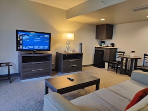 Ein modernes Wohnzimmer mit Flachbildfernseher, Couchtisch, Sofa, Lampe und einer Küchenzeile.