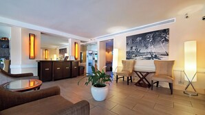 A hotel lobby with a reception desk, seating area, and a large painting of a beach scene. - Large Studio w/ Pool sleeps six in comfort PLUS FREE PARKING INCLUDED! (Honolulu)