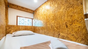 Une pièce avec un mur en bois, une fenêtre, un lit avec une literie blanche et une serviette enroulée posée sur le lit.