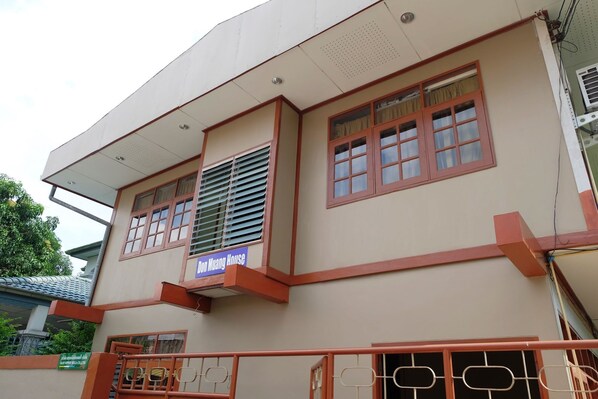 Un edificio de dos pisos con un balcón, un letrero que dice "Ben Muang House" y una entrada con rejas.