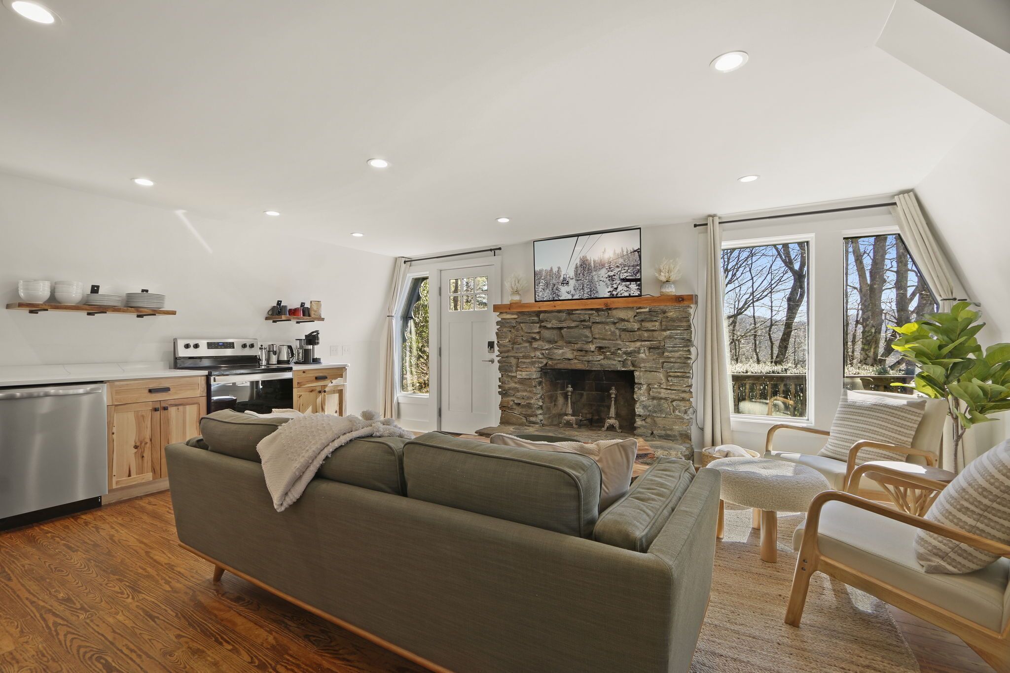 A modern living room with a stone fireplace, wooden furniture, and a kitchen in the background.