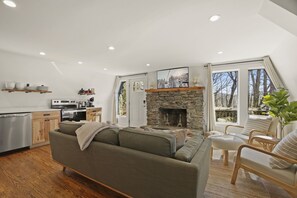 A modern living room with a stone fireplace, wooden furniture, and a kitchen in the background. - A-Frame in the heart of Boone (Boone)