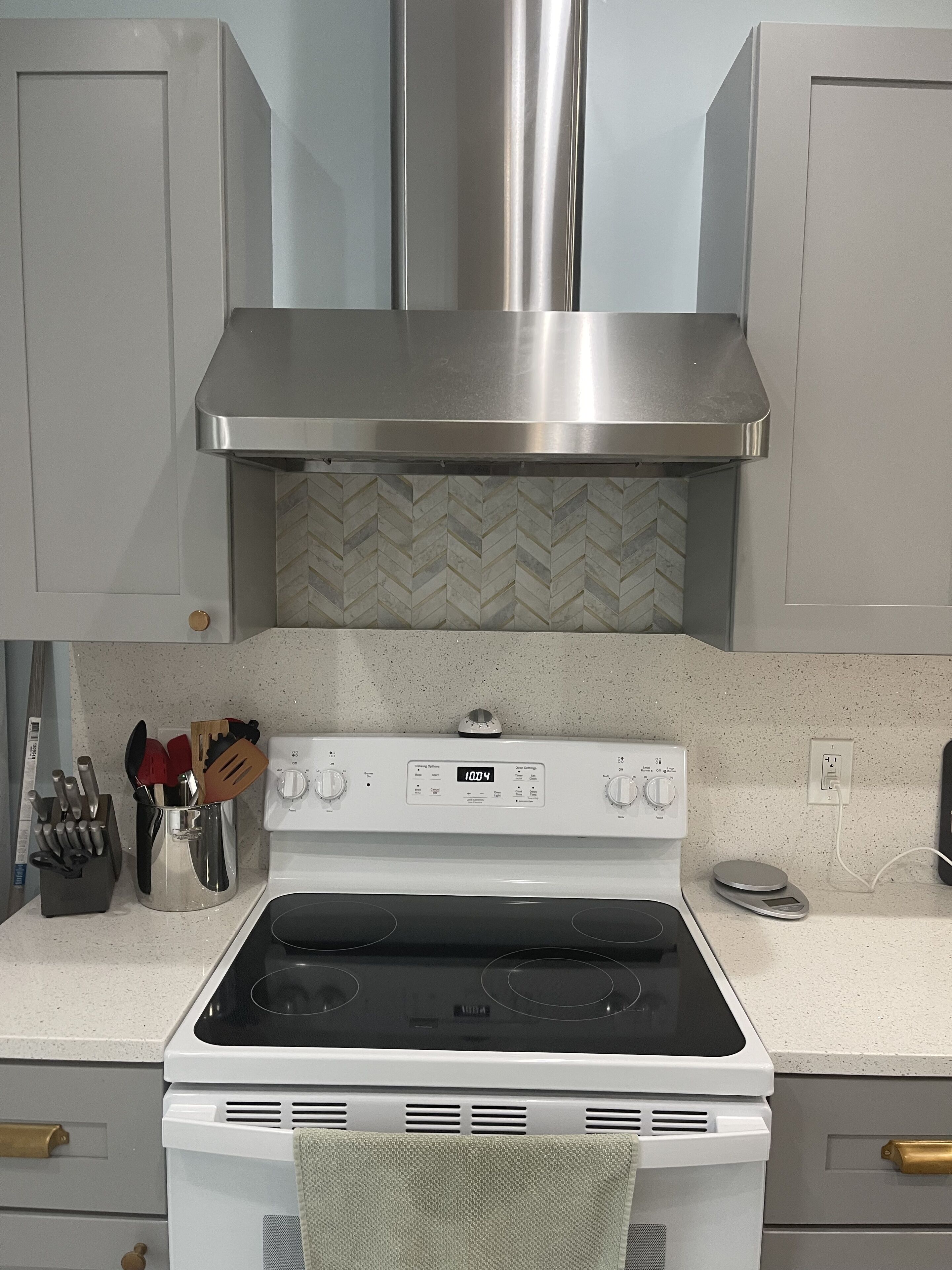 A kitchen with a white stove, stainless steel range hood, and a herringbone tile backsplash.