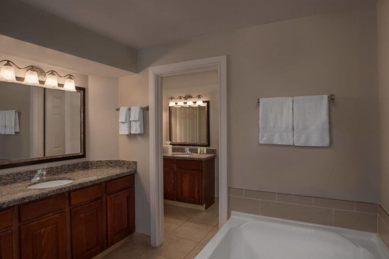 Une salle de bain moderne avec un lavabo sur un plan de travail en granit, des meubles en bois, un grand miroir et une baignoire.