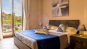 A bedroom with a bed, nightstands, a view through a sliding door, and a painting on the wall. - Villetta Desiderio Apartment (Giardini Naxos)