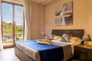 A bedroom with a bed, nightstands, a view through a sliding door, and a painting on the wall. - Villetta Desiderio Apartment (Giardini Naxos)