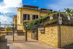 Una entrada cerrada a un edificio residencial con un muro de piedra, una puerta metálica y un letrero de no estacionamiento.