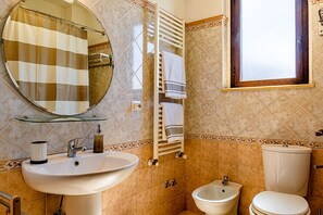 Une salle de bain avec un miroir rond, un lavabo, un bidet et des toilettes.