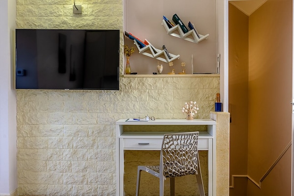 A modern room with a white desk, a mounted TV, and a decorative shelf with books and vases.