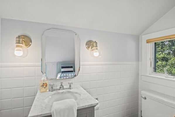 A bathroom with white tiled walls, a marble sink, a large mirror, and two wall-mounted light fixtures.