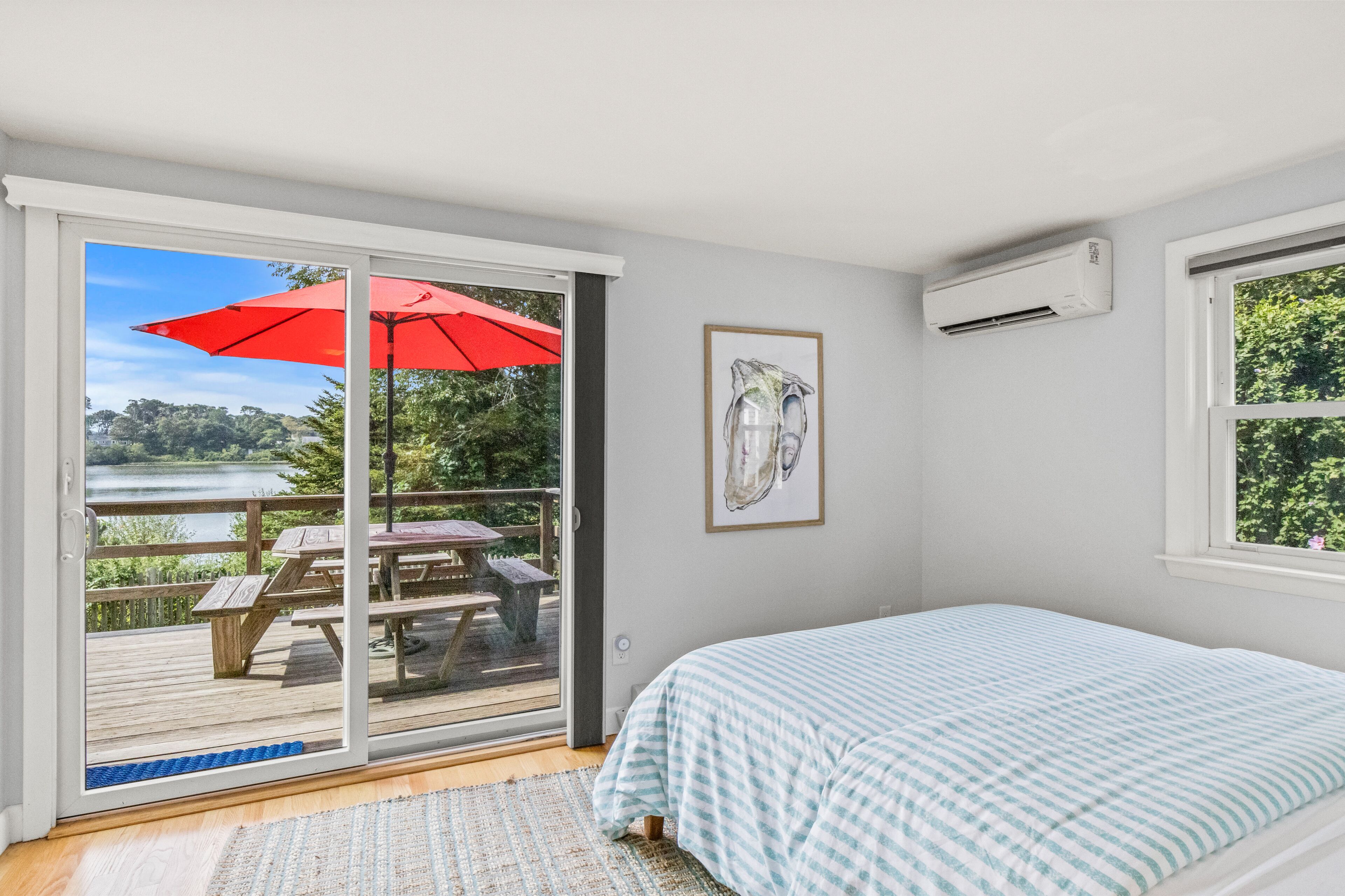 A bedroom with a large sliding glass door leading to a deck with a red umbrella, a framed picture on the wall, and an air conditioning unit.