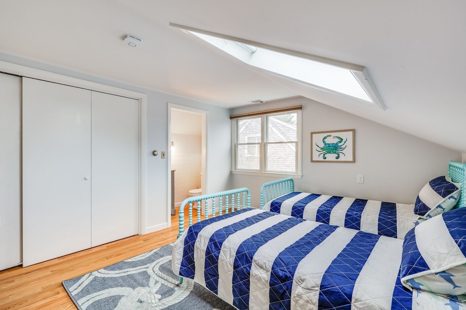 A bedroom with a skylight, a bed with blue and white bedding, a window, and a door leading to a bathroom.