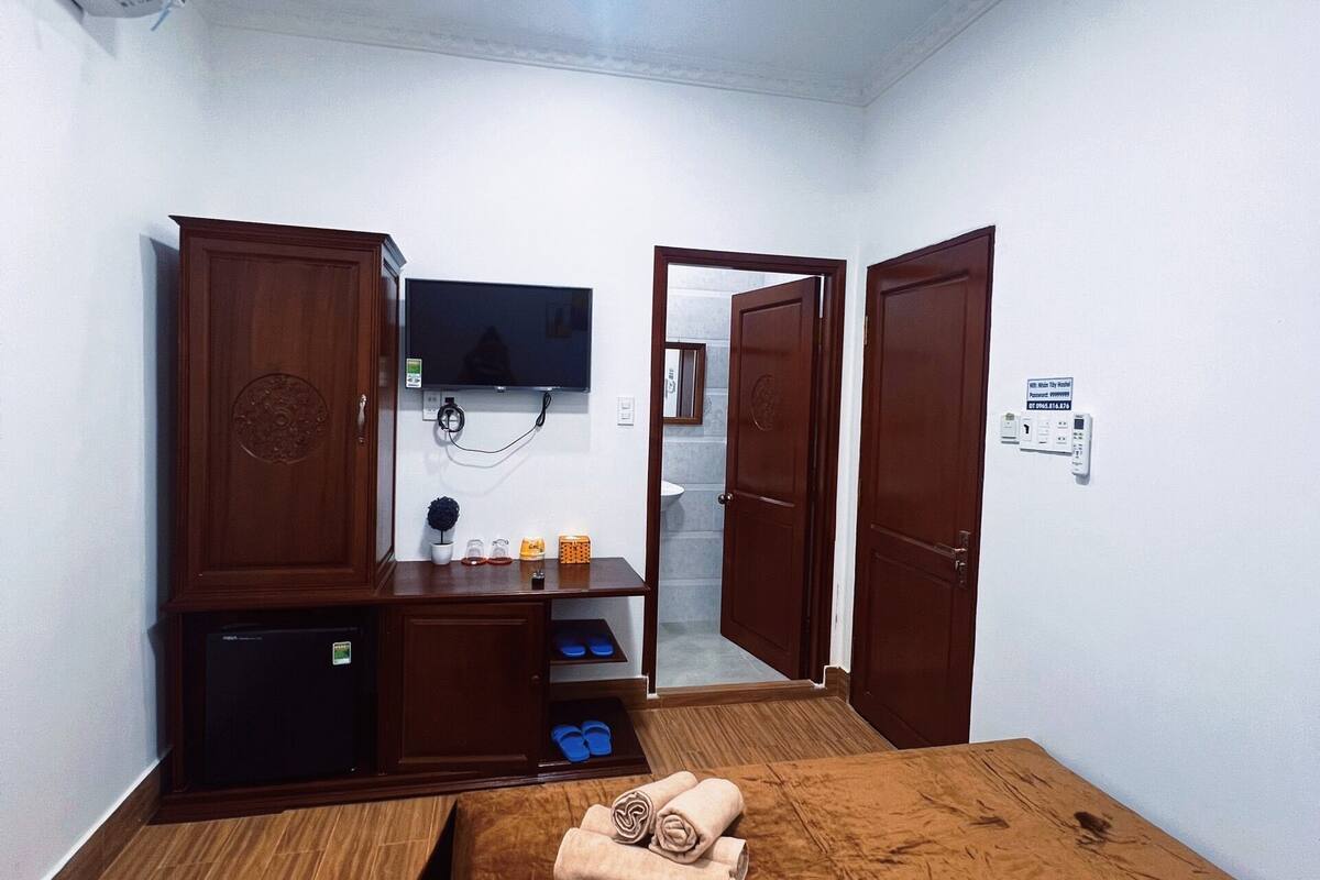 Une chambre de taille modeste, comprenant un lit, une télévision, une armoire et un petit bureau avec une lampe.