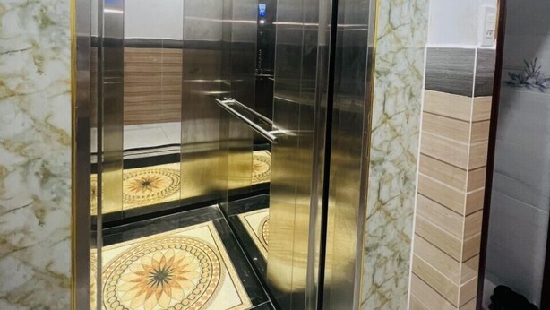 An elevator with a glass door and a metallic interior, featuring a patterned floor design. - Nhan Tay Hostel (Can Tho)