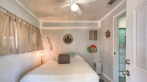 A bedroom with a bed, a ceiling fan, a wall clock, and a small window. - Bahama Waves (Jamaica Beach)