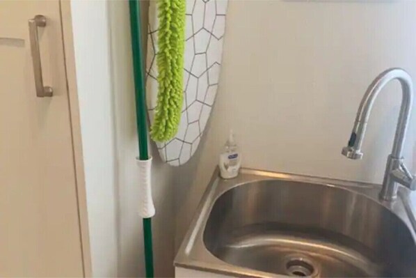 A stainless steel sink with a green towel hanging on a white towel rack, a white bottle of hand soap, and a silver faucet.