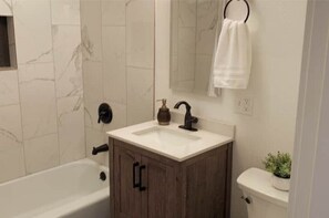 A bathroom with a white marble wall, a wooden cabinet with a sink, a black faucet, a white toilet, and a towel hanging on a ring. - Walk to downtown and only a block from the river! (Bend)
