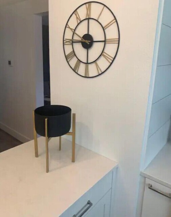 A modern kitchen with a white countertop, a black circular object on a stand, and a wall-mounted clock. - Walk to downtown and only a block from the river! (Bend)