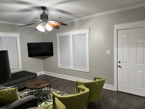 A living room with a ceiling fan, a flat-screen TV, a sofa, two armchairs, and a coffee table.