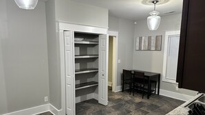 A modern kitchen with dark tiled flooring, a built-in white pantry, a dining area with a table and chairs, and a pendant light above the counter. - Hickory Landing (Nashville)