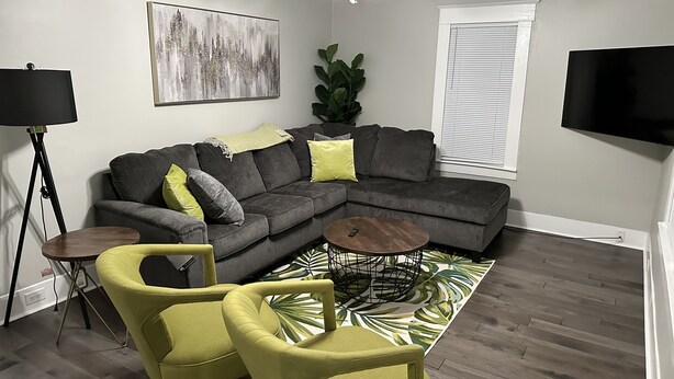 A living room with a sectional sofa, a coffee table, and two armchairs. There is a ceiling fan, a floor lamp, and a large painting on the wall. - Hickory Landing (Nashville)