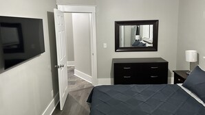 A bedroom with a bed, a dresser, a TV, a mirror, and a door leading to another room. - Hickory Landing (Nashville)