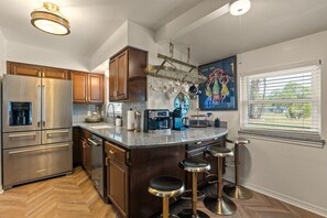 A modern kitchen with stainless steel appliances, a bar area with stools, and a large window with blinds.