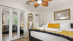 A hotel room with a bed, a ceiling fan, a large mirror, and a framed picture on the wall.