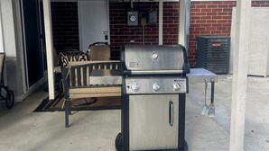 A covered outdoor area with a grill, a sofa, and a brick wall in the background.