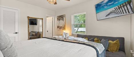 A bedroom with a bed, a ceiling fan, a painting, and a window.