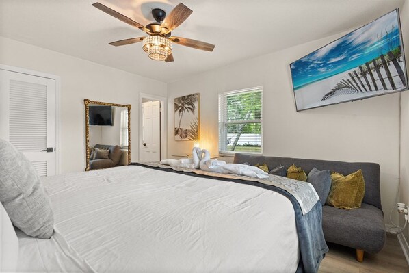A bedroom with a bed, a ceiling fan, a painting, and a window.
