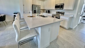 Una cocina moderna con armarios blancos, electrodomésticos de acero inoxidable y una isla central con taburetes de bar.