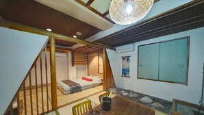 A traditional Japanese-style room with tatami flooring, a low wooden bed, a dining table with a bottle, and a hanging light fixture. - HOTEL IS (Yokohama)