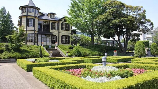 A large, multi-story building with a turret and a formal garden with hedges and flower beds. - HOTEL IS (Yokohama)