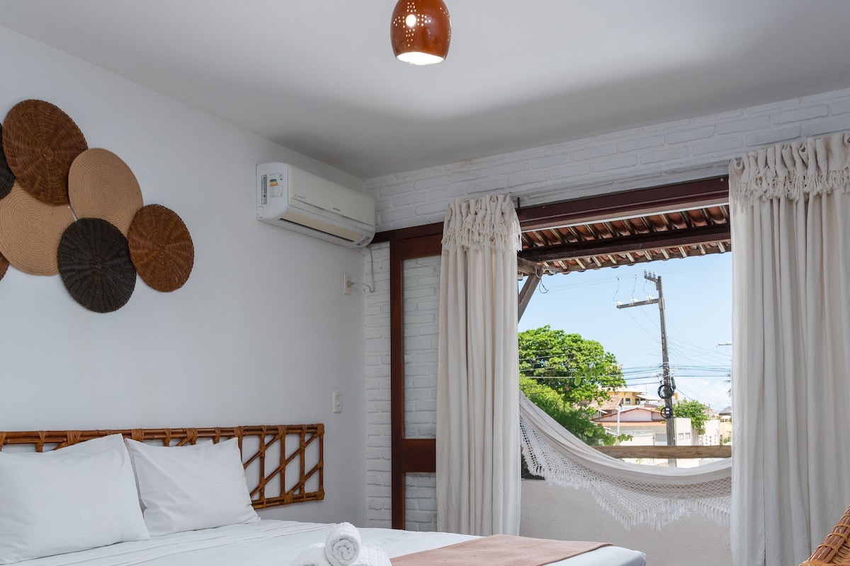 Une chambre d’hôtel avec un lit, des rideaux blancs, un hamac et une vue sur la mer.