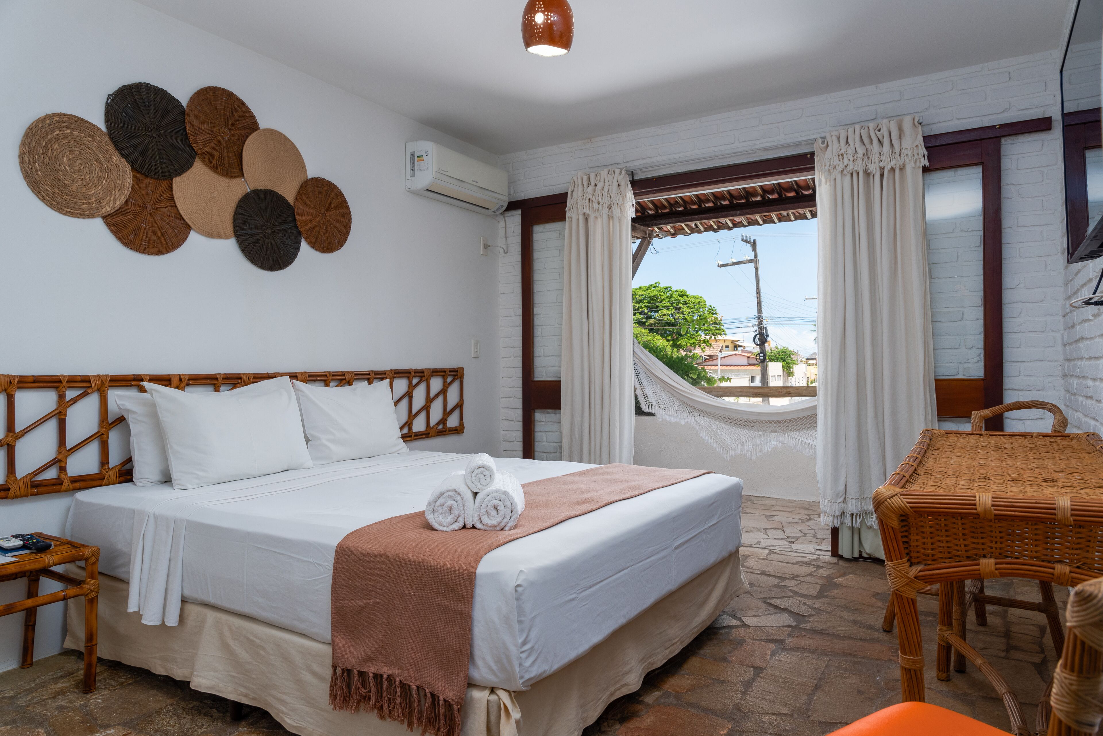 Habitació d'hotel amb un llit, una cadira de vimetla, una taula i vista a l'exterior.