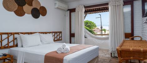 A hotel room with a bed, a wicker chair, a table, and a view of the outdoors.